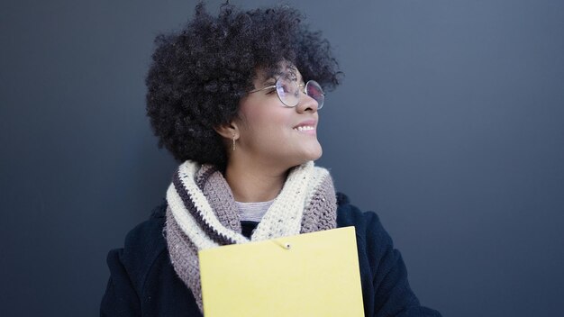 Young african american woman smiling confident holding folder over isolated black background