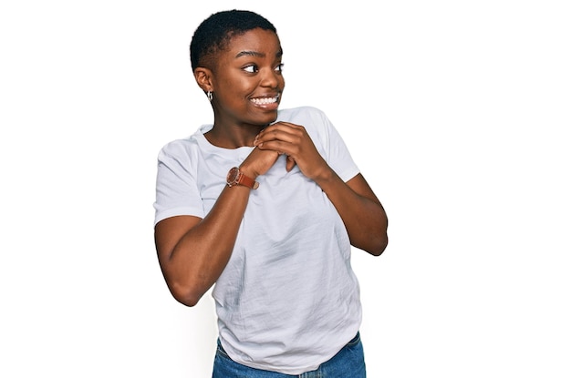 Young african american woman wearing casual white t shirt laughing nervous and excited with hands on chin looking to the side