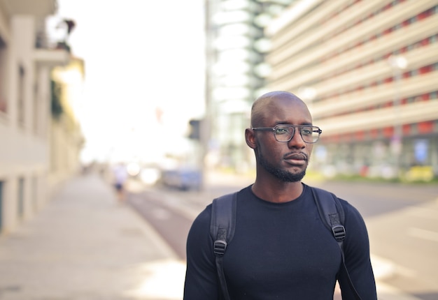 Young African male with glasses wearing a black t-shirt and a backpack in the street