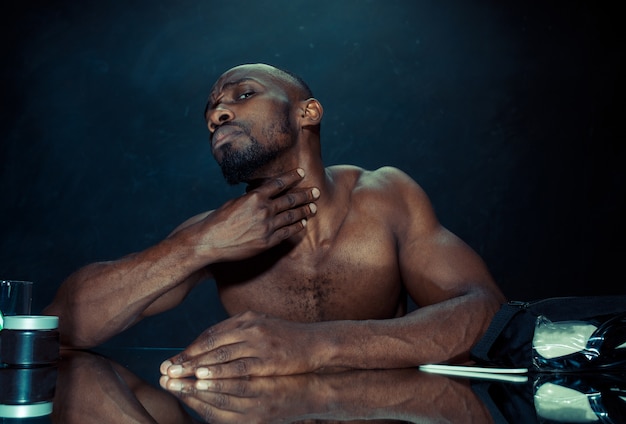 The young african man in bedroom sitting in front of the mirror after scratching his beard at home. Human emotions concept