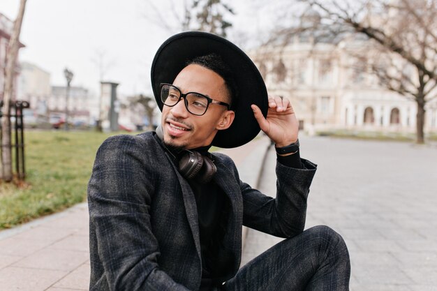 Young african man enjoying good spring day in park. Outdoor photo of amazing mulatto male model sitting in square and waiting someone.