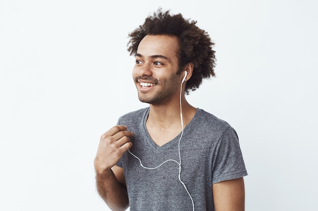 Free photo young african man smiling putting out one wired headphone over white wall listening to birds.