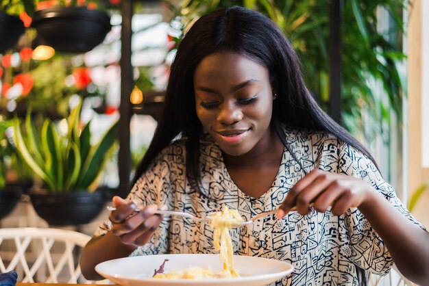 Young african woman eating spaghetti in restaurant