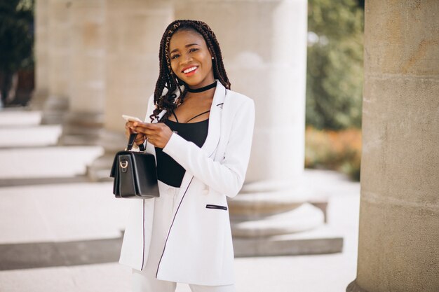 Young african woman in white suit using phone