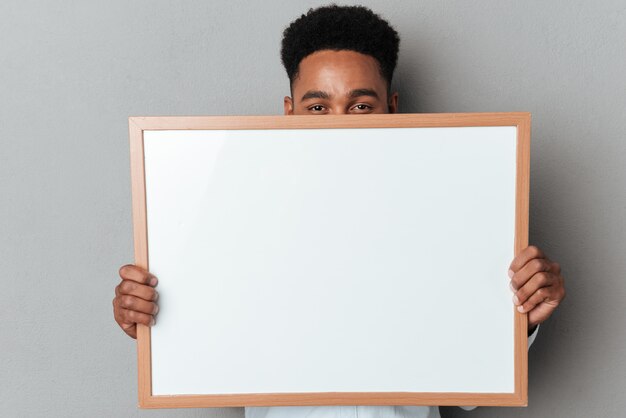 Young afro american man hiding behind blank board