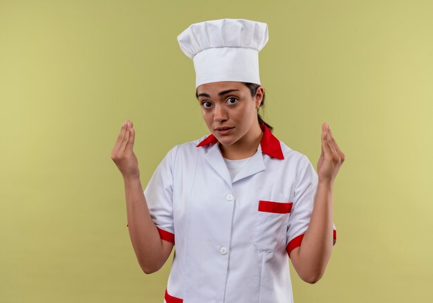 Young anxious caucasian cook girl in chef uniform holds hands up isolated on green background with copy space