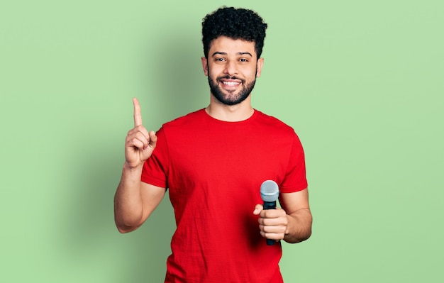 Free Photo young arab man with beard singing song using microphone smiling with an idea or question pointing finger with happy face, number one