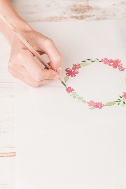 Young artist drawing flowers pattern with watercolor paint and brush on paper at workplace