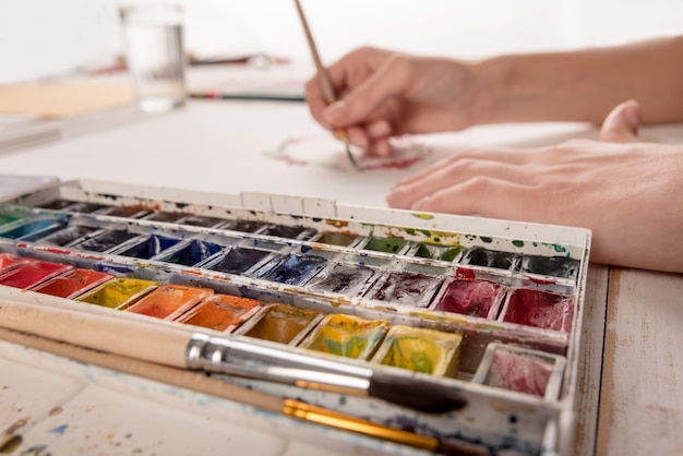 Young artist drawing flowers pattern with watercolor paint and brush at workplace