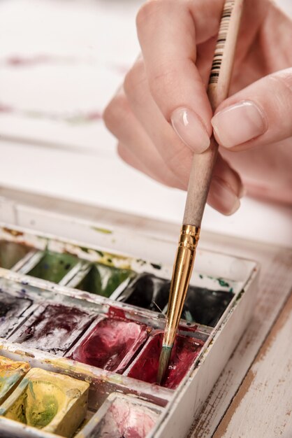 Young artist drawing flowers pattern with watercolor paint and brush at workplace