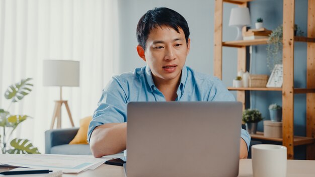 Young Asia businessman using laptop talk to colleagues about plan in video call while smart working from home