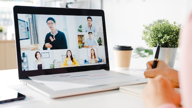 Free photo young asia businesswoman using laptop talk to colleague about plan in video call meeting while work from home at living room.