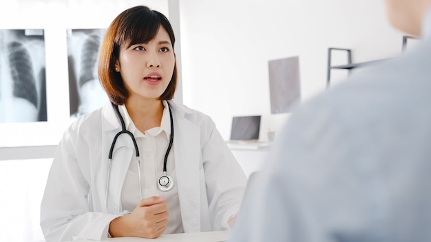 Young Asia female doctor in white medical uniform using computer laptop is delivering great news talk discuss results