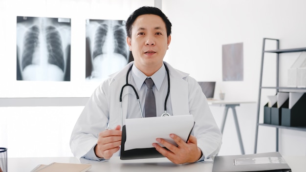 Free Photo young asia male doctor in white medical uniform with stethoscope using computer laptop talk video conference call with patient, looking at camera in health hospital.