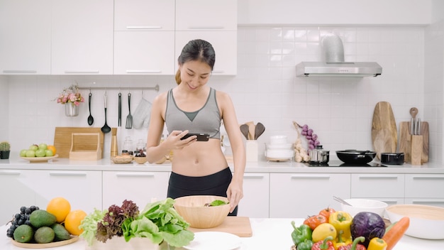 Young Asian blogger woman using smartphone photo post in social media in the kitchen