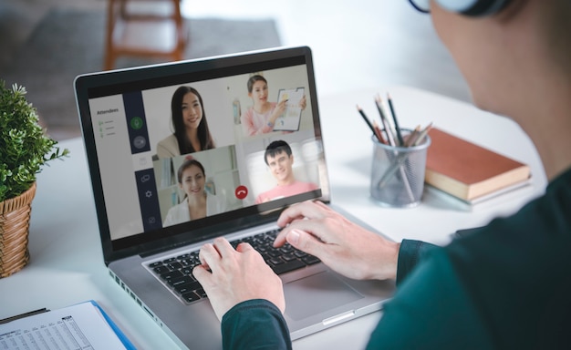 Young Asian businessman wear headphones working remotely from home and virtual video conference meeting with colleagues business people. social distancing at home office concept.