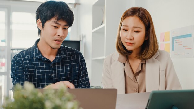 Young asian creative businessman and businesswoman manager discuss project compare point in paperwork and laptop