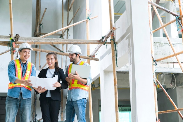 Young Asian engineers teamwork site inspector and discuss together using notebook computer and paper blueprint at building construction sitehome renovation ideas concept