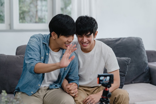 Young Asian gay couple influencer couple vlog at home. Teen korean LGBTQ men happy relax fun using camera record vlog video upload in social media while lying sofa in living room at house .