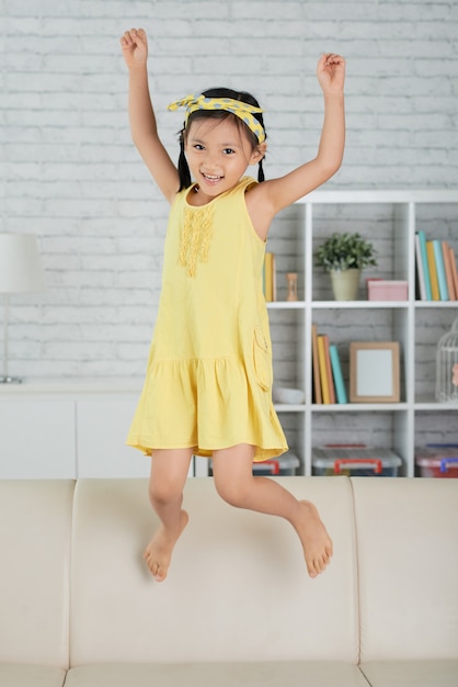 Young Asian girl jumping on sofa at home and laughing