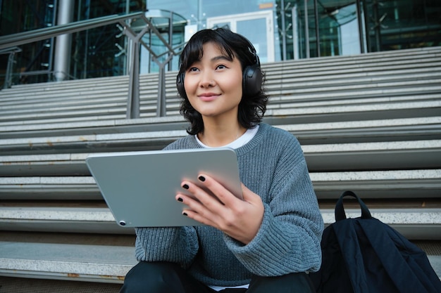 Young asian girl student in headphones works on remote digital artist drawing on tablet with graphic