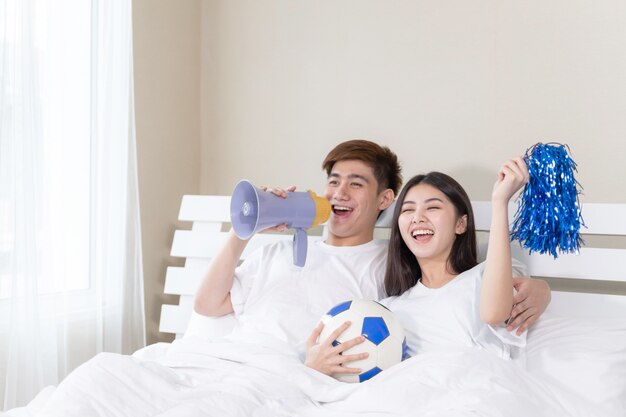 Young Asian handsome husband and beautiful wife feel great cheering for their team