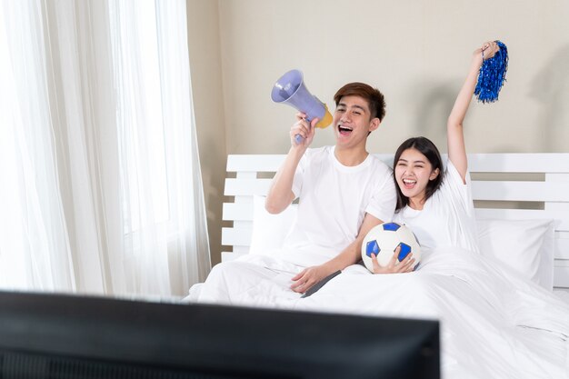 Young Asian handsome husband and beautiful wife feel great cheering for their team