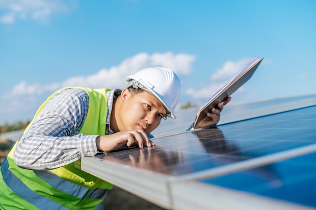 Young Asian Inspector Engineer man working at solar farm Technician or supervisor male in white helmet Checking operation of sun and photovoltaic solar panel in station copy space