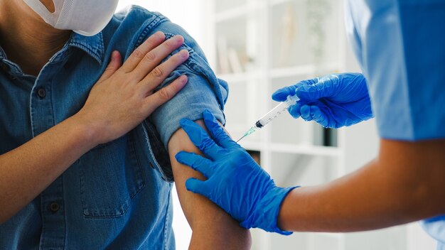 Young asian lady nurse giving Covid-19 or flu antivirus vaccine shot to senior male patient