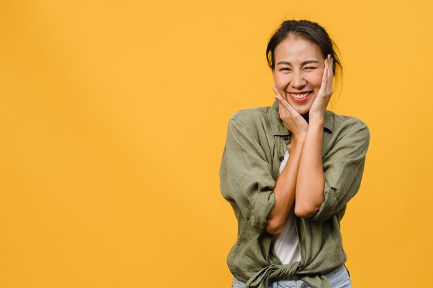 Young Asian lady with positive expression, smile broadly, dressed in casual clothing  over yellow wall. Happy adorable glad woman rejoices success. Facial expression concept.