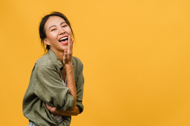 Young Asian lady with positive expression, smile broadly, dressed in casual clothing  over yellow wall. Happy adorable glad woman rejoices success. Facial expression concept.