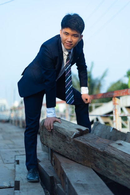 Free photo young asian man in a suit crouched on a a pile of logs