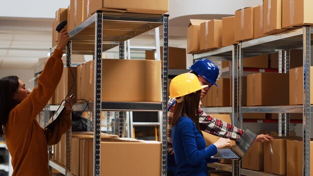 Young asian people looking at carton boxes on racks, checking merchandise stock in storage room. Man and woman using laptop to work on products distribution, business development.