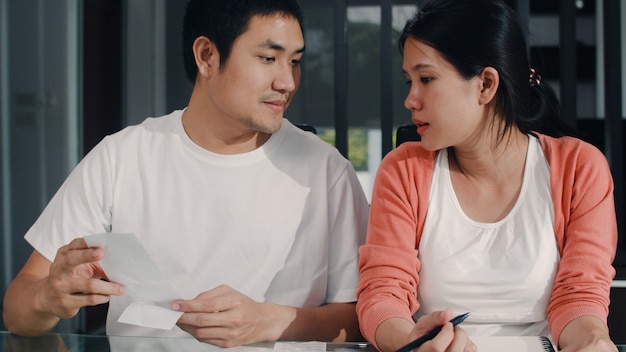 Young Asian Pregnant couple records of income and expenses at home. Mom and Dad happy using laptop record budget, tax, financial document, e commerce working in living room at home .