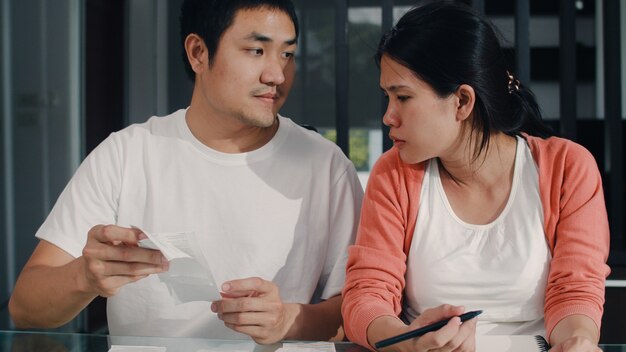 Young Asian Pregnant couple records of income and expenses at home. Mom and Dad happy using laptop record budget, tax, financial document, e commerce working in living room at home .