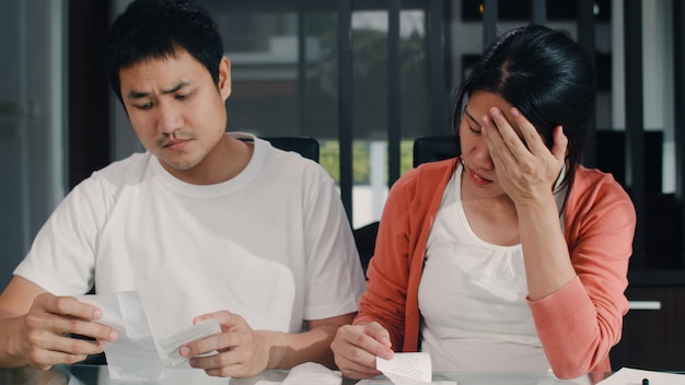 Young Asian Pregnant couple records of income and expenses at home. Mom worried, serious, stress while record budget, tax, financial document working in living room at home .