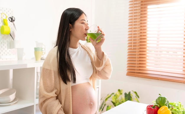 Young Asian pregnant woman drinking green vegetable juice in kitchen room eating to maintain good health during pregnancy until near childbirth