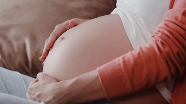 Young Asian Pregnant woman holding her belly talking with her child. Mom feeling happy smiling positive and peaceful while take care baby, pregnancy lying on sofa in living room at home .