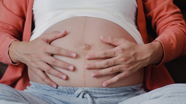 Young Asian Pregnant woman holding her belly talking with her child. Mom feeling happy smiling positive and peaceful while take care baby, pregnancy lying on sofa in living room at home .