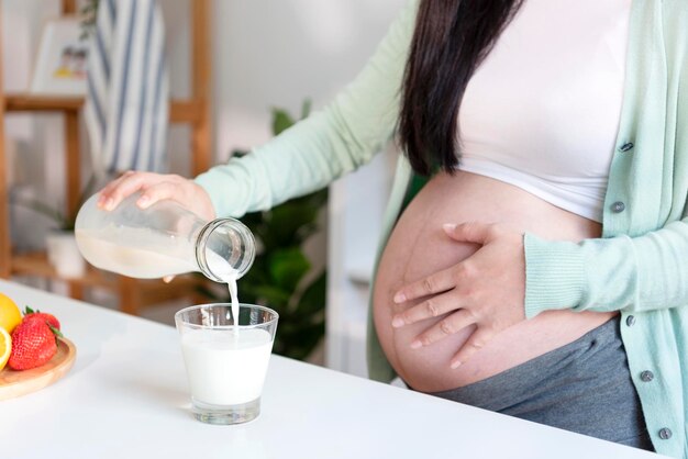 Young Asian pregnant woman standing in kitchen room holding a glass of fresh milk