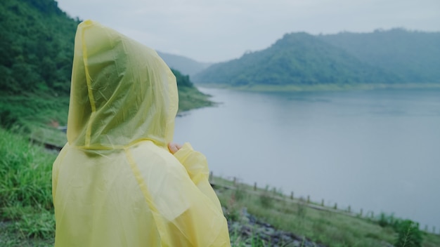 Young Asian woman feeling happy playing rain while wearing raincoat standing near lake