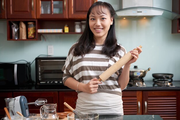 Young Asian woman posing in kitchen at home with baking utensils