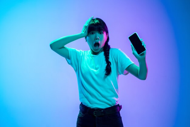 Young asian woman's portrait on gradient blue-purple studio background in neon light. Concept of youth, human emotions, facial expression, sales, ad. Beautiful brunette model.