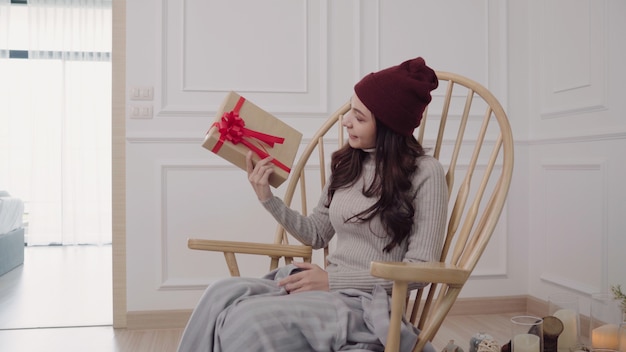 Young Asian woman sitting on a chair wrapped in grey blanket in her living room at home. 