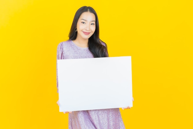 Free Photo young asian woman with empty white billboard on yellow