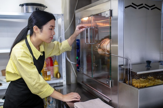 Free photo young asian woman working in the kitchen and regulating ovens temperature