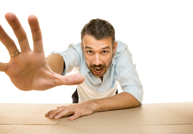 Young astonished man opening the biggest postal package isolated on white wall