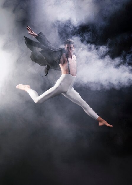 Young athletic male jumping with extended legs and hands near smoke