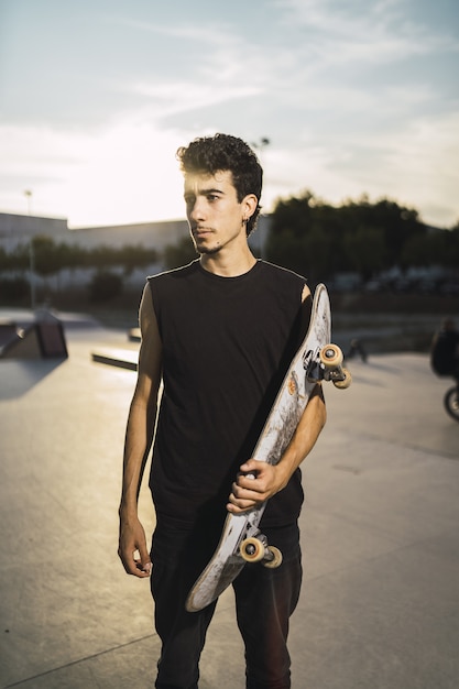 Free photo young athletic male with a black shirt holding a skateboard looking aside