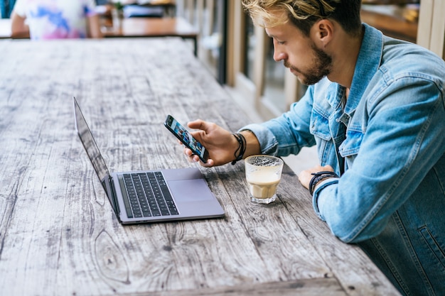 Free Photo young attractive business man in a cafe works for a laptop, drinks coffee.